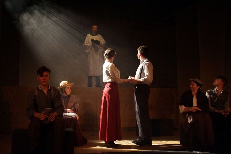 Two actors stand facing each other on stage